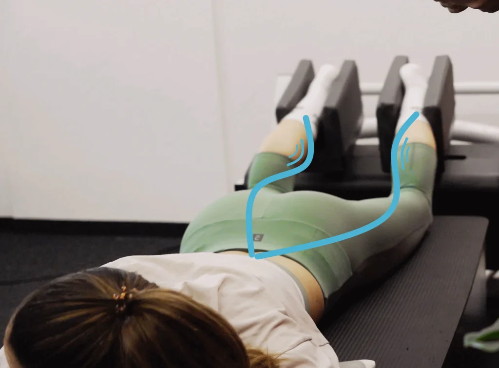 Persona en posición de entrenamiento con piernas sujetas en dispositivo especializado con tecnología de Onda cinética, representando innovación en salud y rendimiento deportivo.