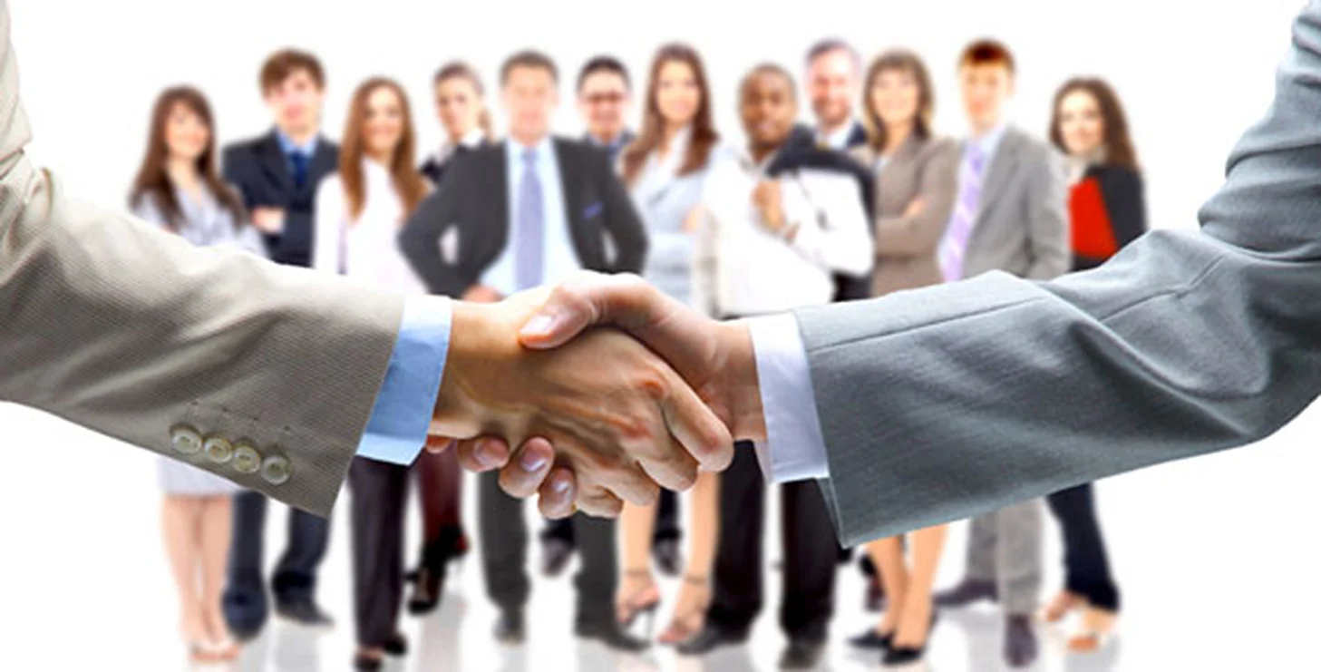 A handshake between professionals with a work team in the background, representing the commitment, collaboration and experience of the ARB Systems team in the development of aesthetic and muscle recovery technology.