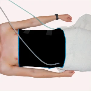 Personne allongée utilisant un échangeur thermique noir à bords bleus au niveau de l'abdomen, relié à des tubes pour la thérapie par le froid ou la chaleur.